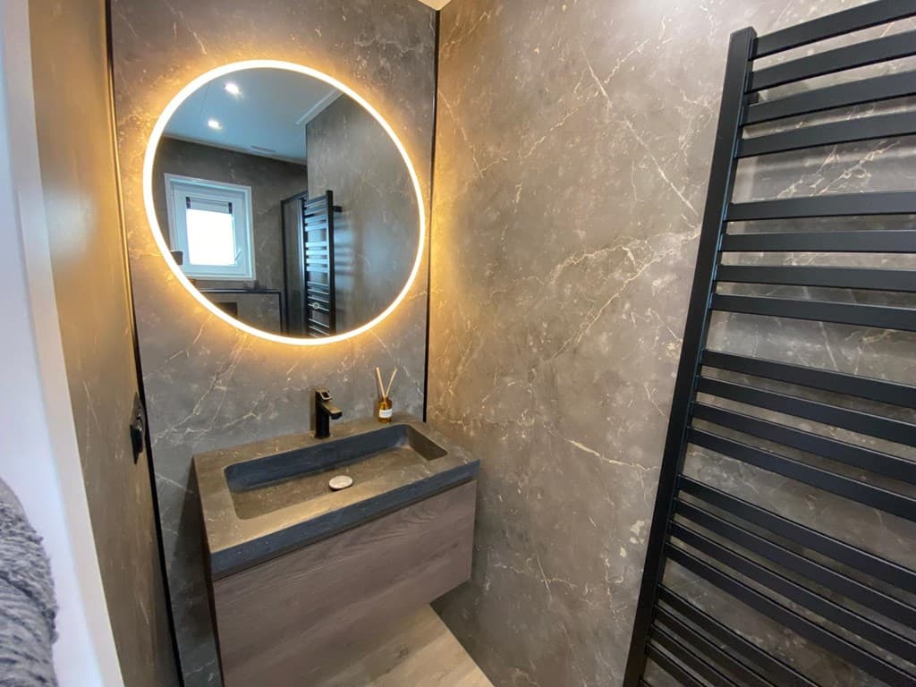 Moderne badkamer met marmeren muren, verlichte spiegel, wastafel en handdoekradiator