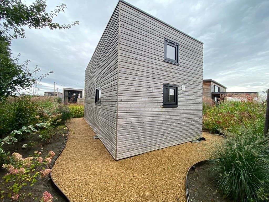 Moderne houten woning omringd door groen en een grindpad, gelegen in een vakantiepark.