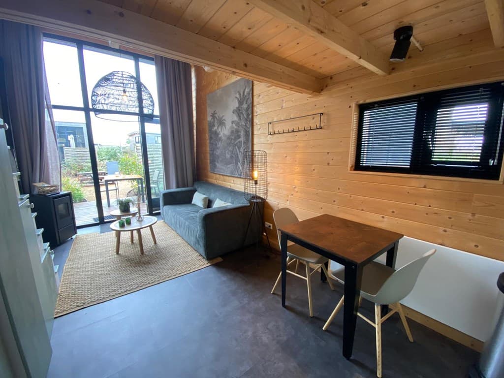 Ruimte met houten wanden, een bank, een eettafel met stoelen en grote ramen met uitzicht op een buitenruimte