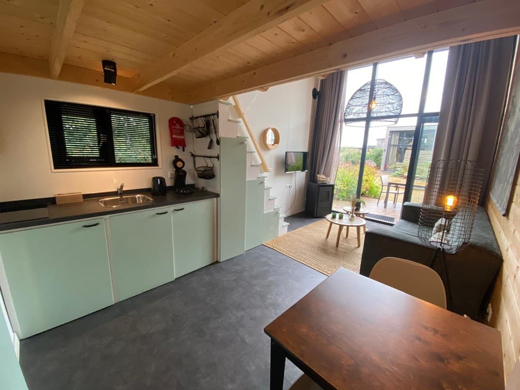 Gezellige woonkamer met open keuken, trap naar boven, eettafel en grote ramen met uitzicht op de buitenruimte