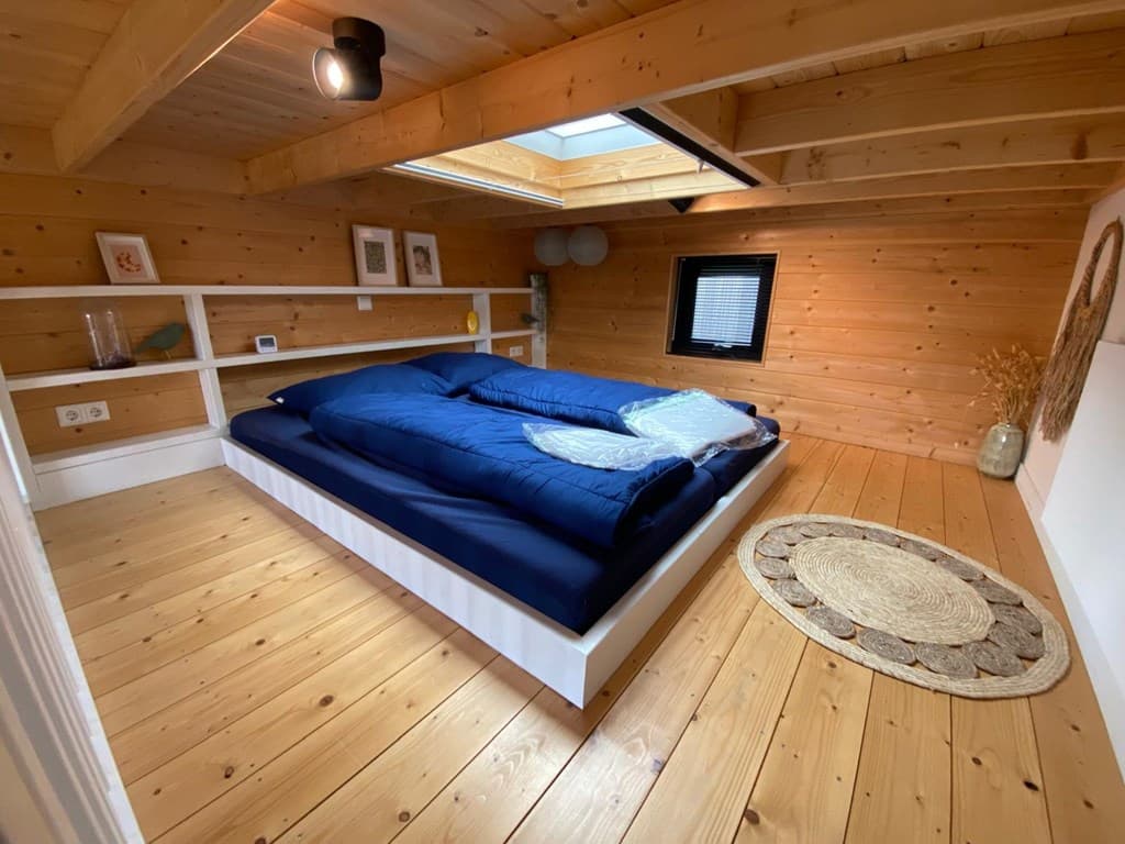 Slaapkamer met houten wanden, groot bed met blauwe dekbedden en een dakraam voor natuurlijke lichtinval.