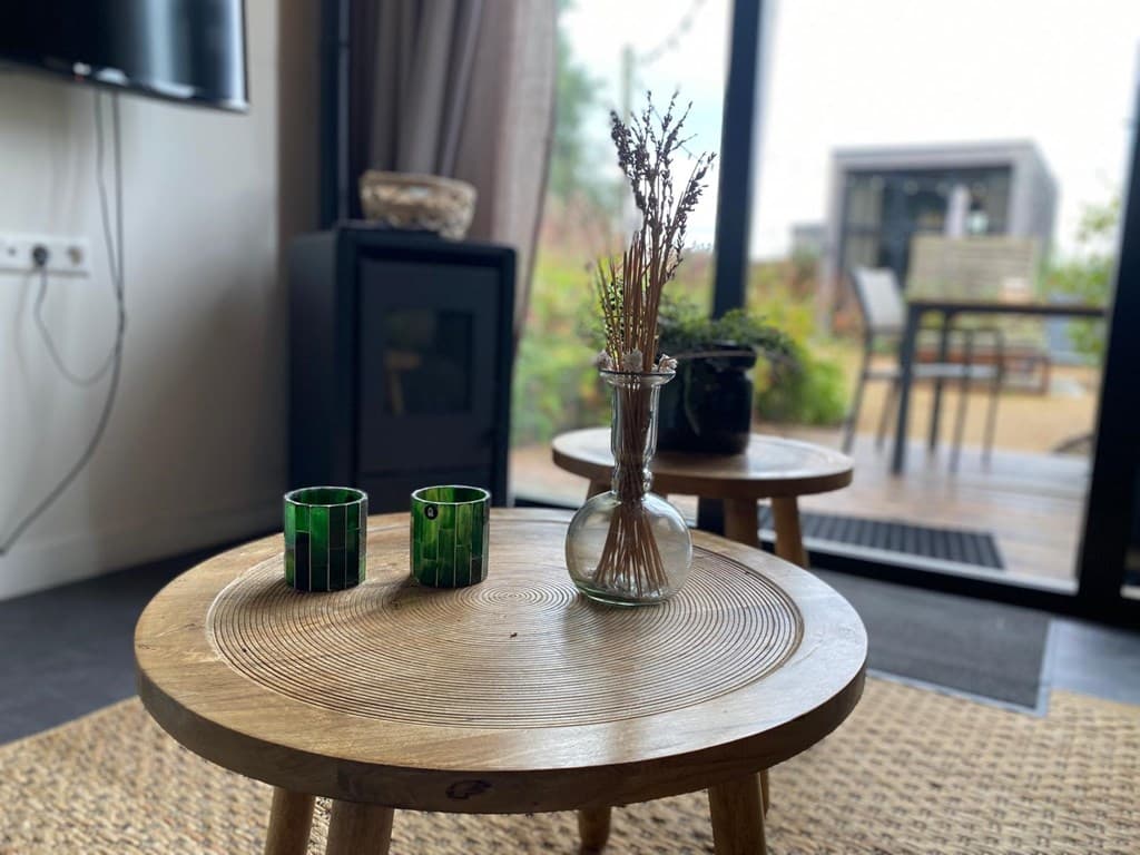 Houten bijzettafels met een vaas en kaarsen in een woonkamer met zicht op een terras en tuin.