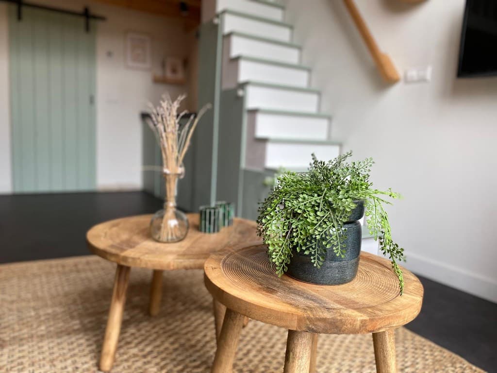 Gezellige zithoek met houten tafels, planten en een trap op de achtergrond in een lichte ruimte