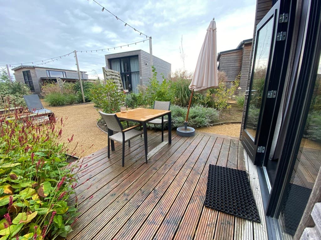 Terras met houten vlonder, tafel en stoelen, zicht op de tuin met planten en andere vakantiehuisjes in de achtergrond