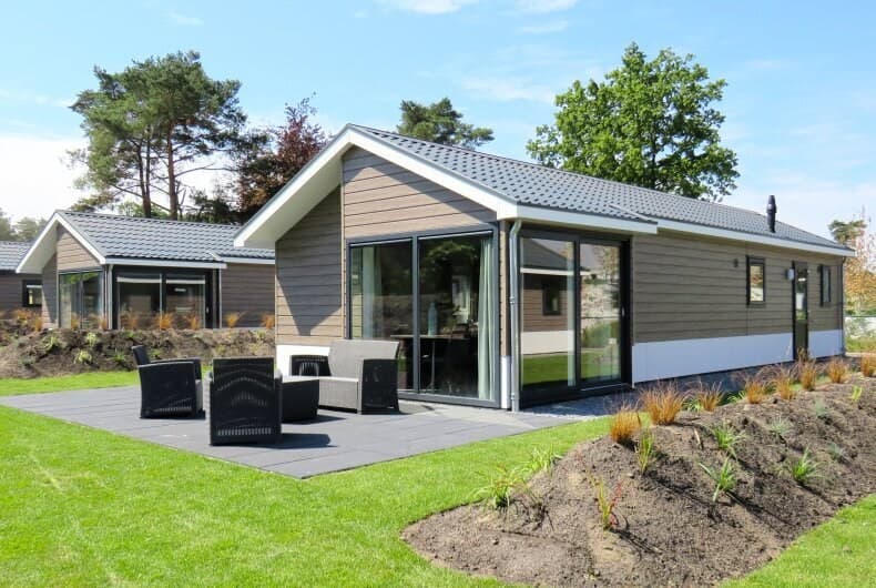Moderne vakantiewoning met een terras en zithoek, omringd door groen en andere woningen in een ruim park.