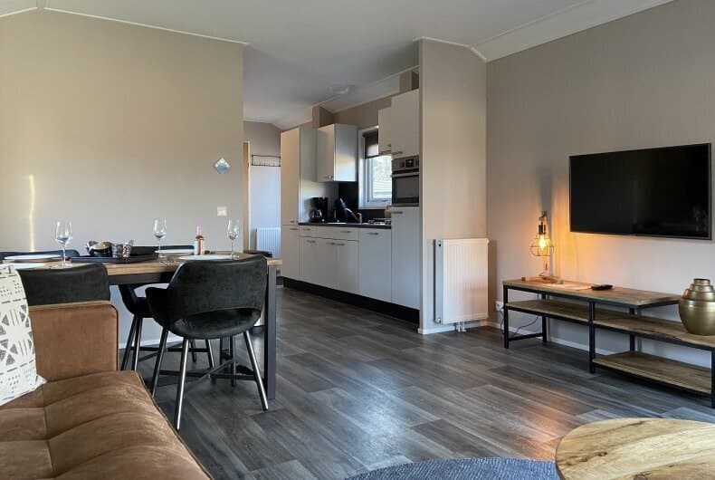 Ruime woonkamer met eettafel, open keuken en zithoek, voorzien van moderne meubels en een tv aan de muur