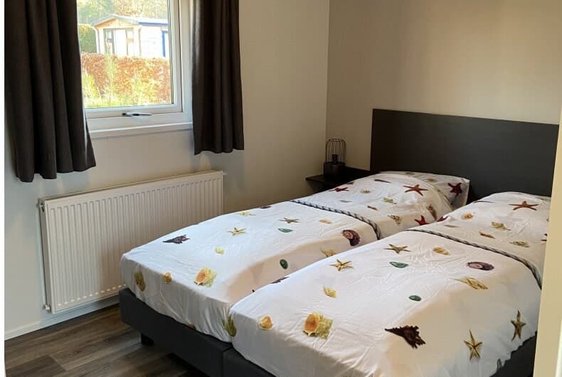 Slaapkamer met twee eenpersoonsbedden en een raam met uitzicht op groen buiten.