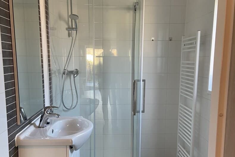 Moderne badkamer met douchecabine, wastafel en handdoekenradiator in lichte wandtegels.