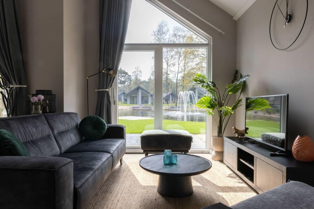 woonkamer met bank en tv-meubel, grote ramen met uitzicht op tuin en fontein, planten in de hoek
