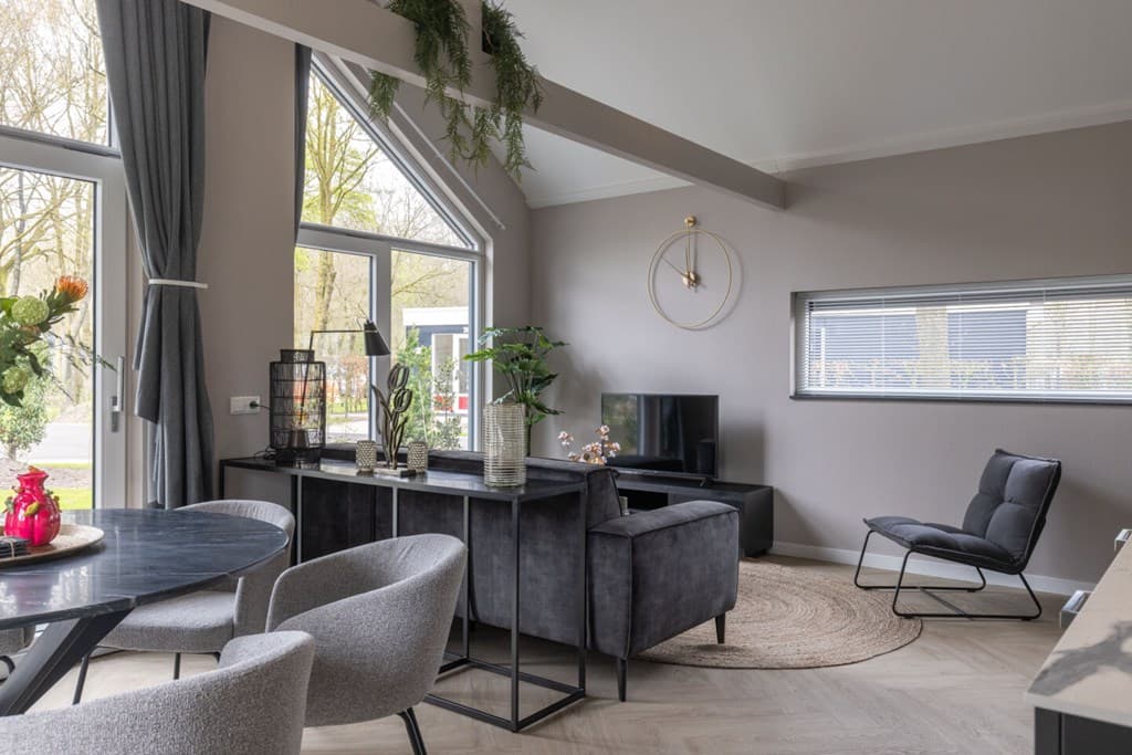Moderne woonkamer met grote ramen, zwarte meubels en een ronde vloerkleed, sfeervol ingericht met planten en decoratie