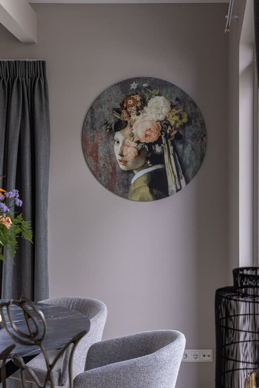 Ronde schilderij met een vrouw met bloemen in het haar aan de muur, grijze gordijnen en comfortabele stoelen zichtbaar.