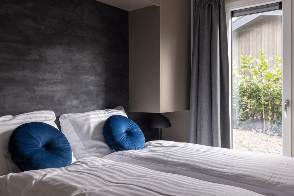 Slaapkamer met twee eenpersoonsbedden, blauwe kussens en ramen met uitzicht op de tuin.