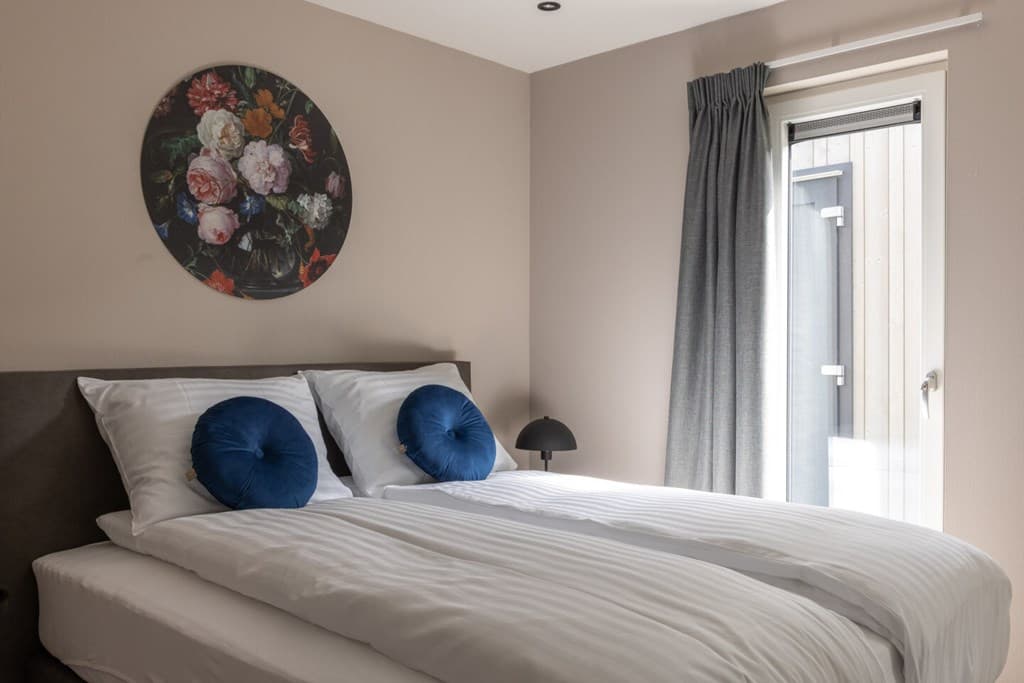 Slaapkamer met een tweepersoonsbed, decoratieve kussens, een schilderij en een deur naar buiten.