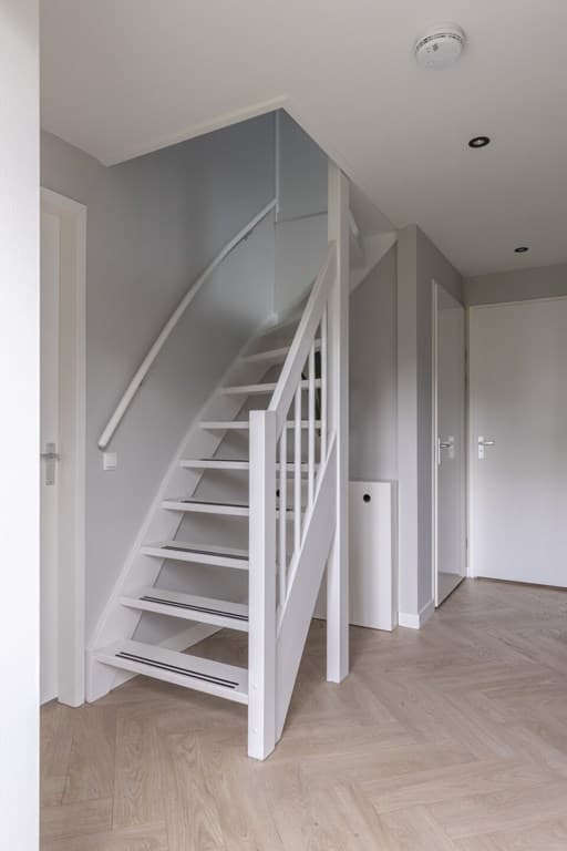 Moderne entree met trap, lichtgrijze wanden en een houten vloer. De ruimte is strak en minimaal ingericht.