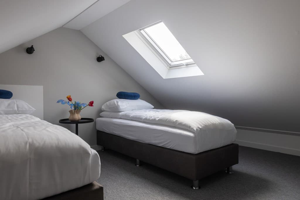 Slaapkamer met twee eenpersoonsbedden, een nachttafel en een dakraam onder een schuine wand
