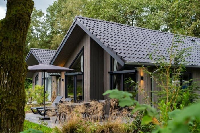 Moderne vakantiewoning met een grijze houten gevel, terrasje en parasol omringd door groen in Vakantiepark Latour.