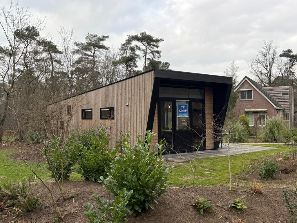 Moderne houten vakantiewoning met grote ramen gelegen in een bosrijke omgeving met groen en gras rond het huis