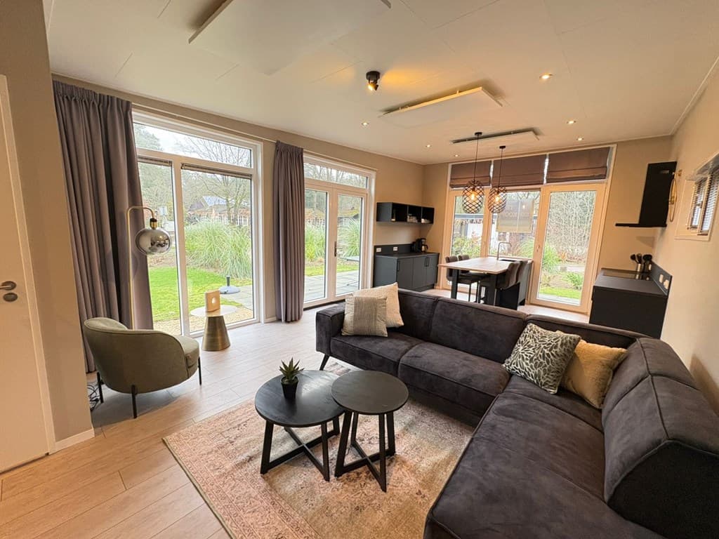 Moderne woonkamer met bank, salontafel en eettafel, grote ramen met uitzicht op de tuin en een rustige inrichting
