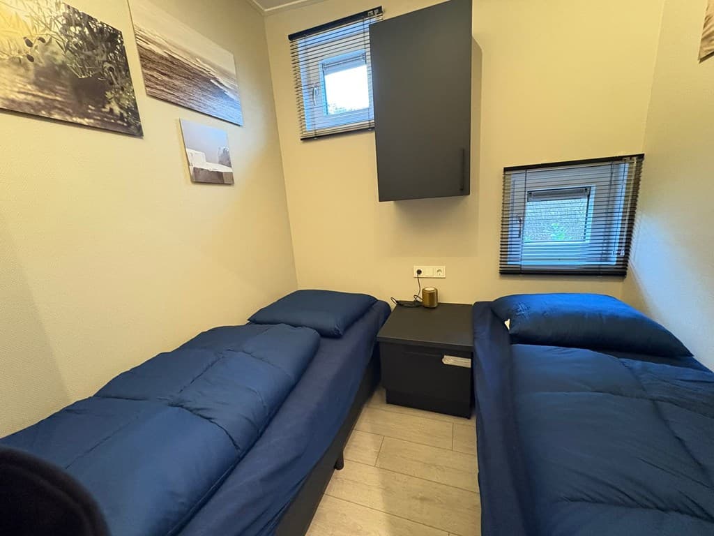 Slaapkamer met twee eenpersoonsbedden, een nachtkastje en ramen met jaloezieën.