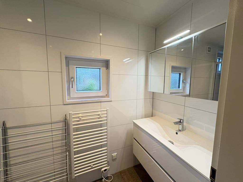 Moderne badkamer met witte tegels, wastafel met spiegel, raam en handdoekenradiator.