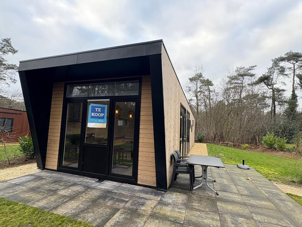 Moderne vakantiewoning met houten gevel, grote ramen en een terras met tafels in een groene omgeving