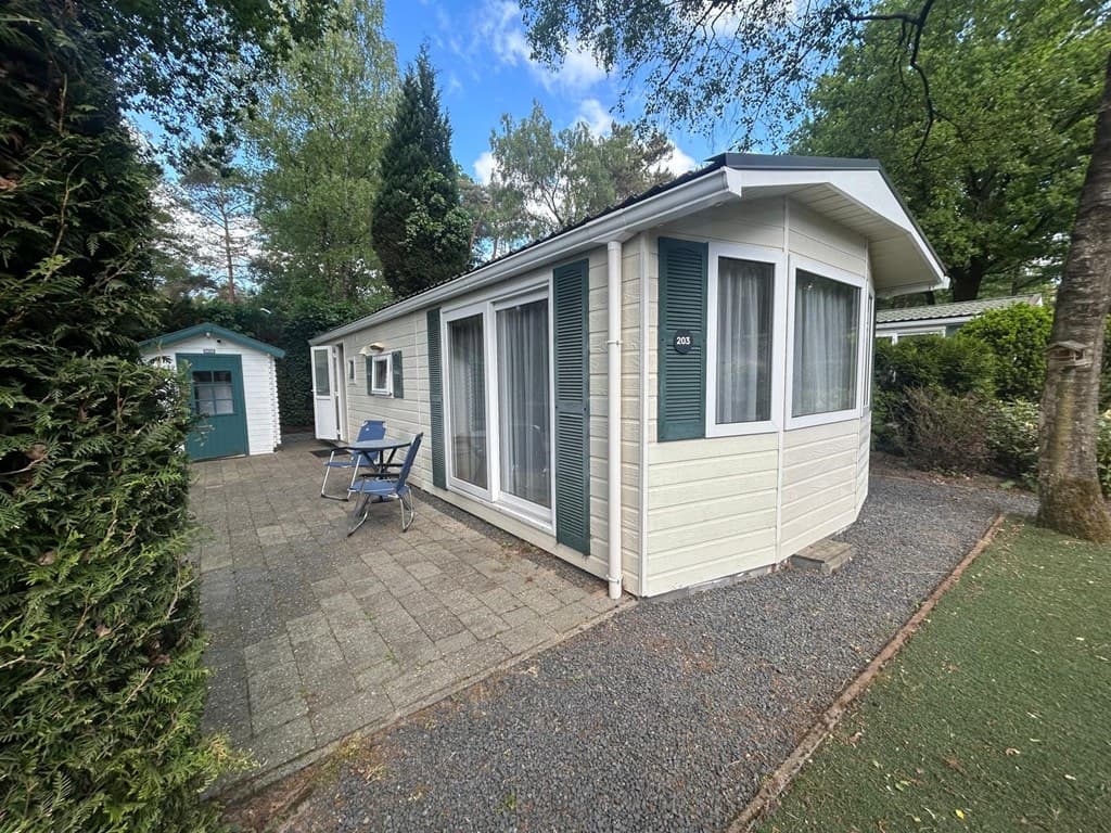 Vakantiehuis met terras en twee stoelen, omringd door bomen en groen, gelegen op een parkachtige omgeving