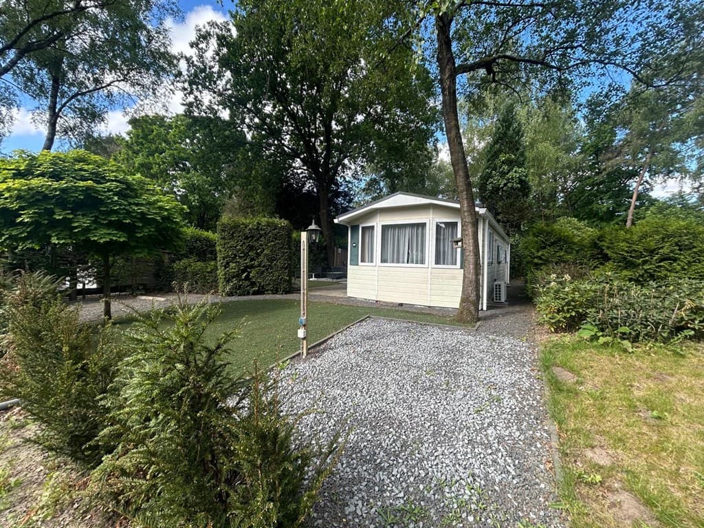 Vakantiehuis in een groene omgeving met een grindpad en aangelegde tuin met bomen en struiken.