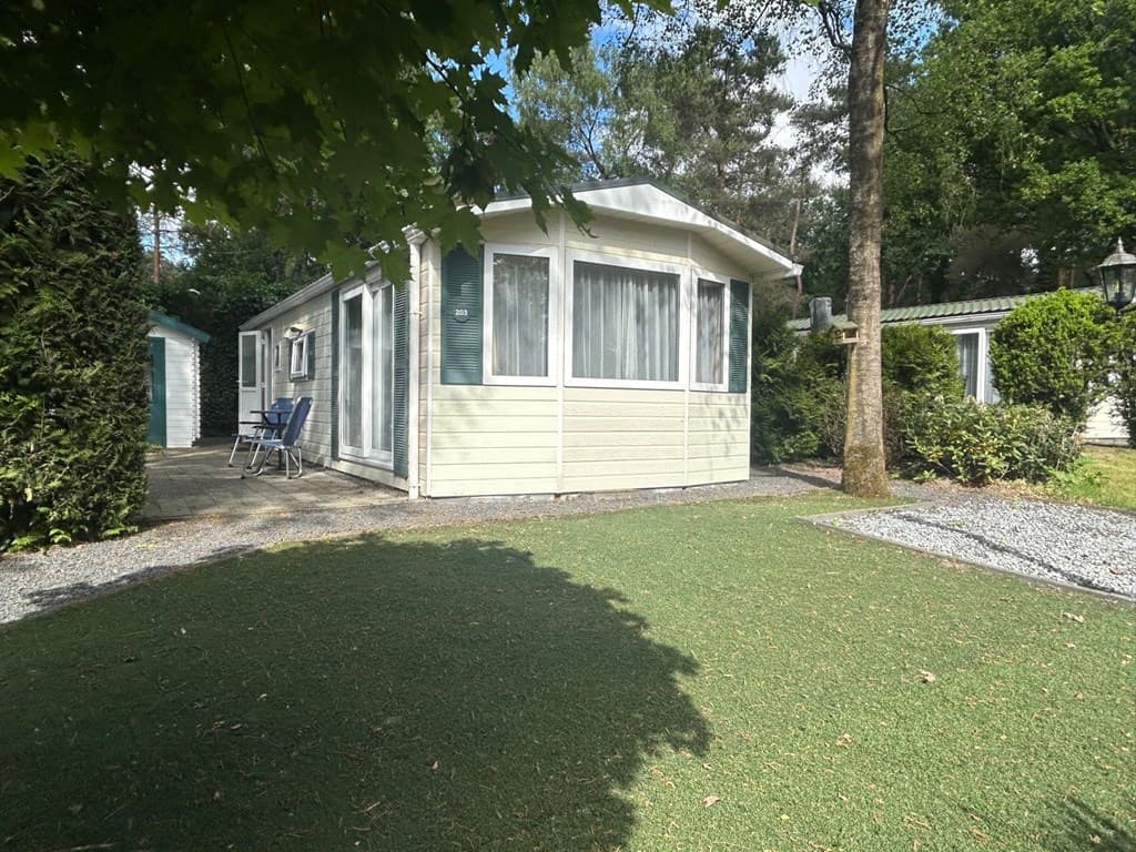 Vakantiewoning met grote ramen, groen grasveld en bomen eromheen, gelegen in een bosrijke omgeving.