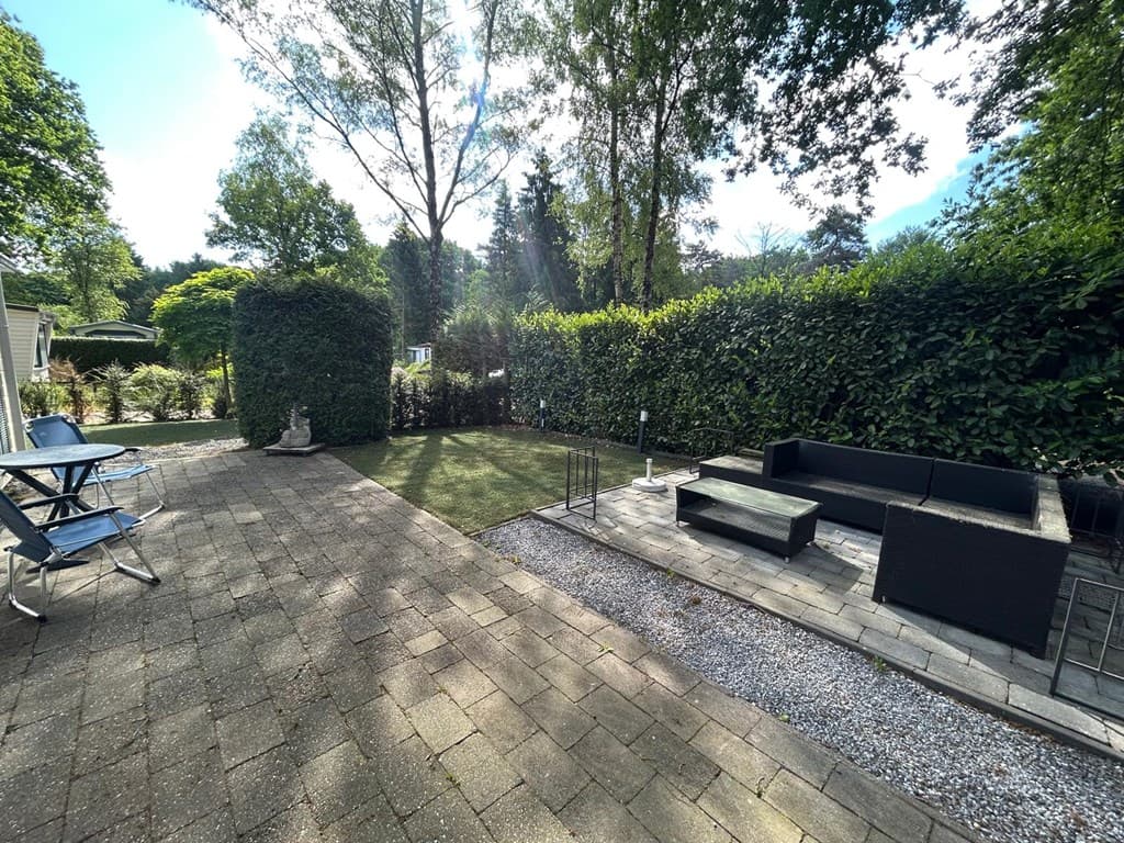 Terras met strakke hardstenen tegels, groene afscheidingen, een zithoek en een grasveld in de tuin.