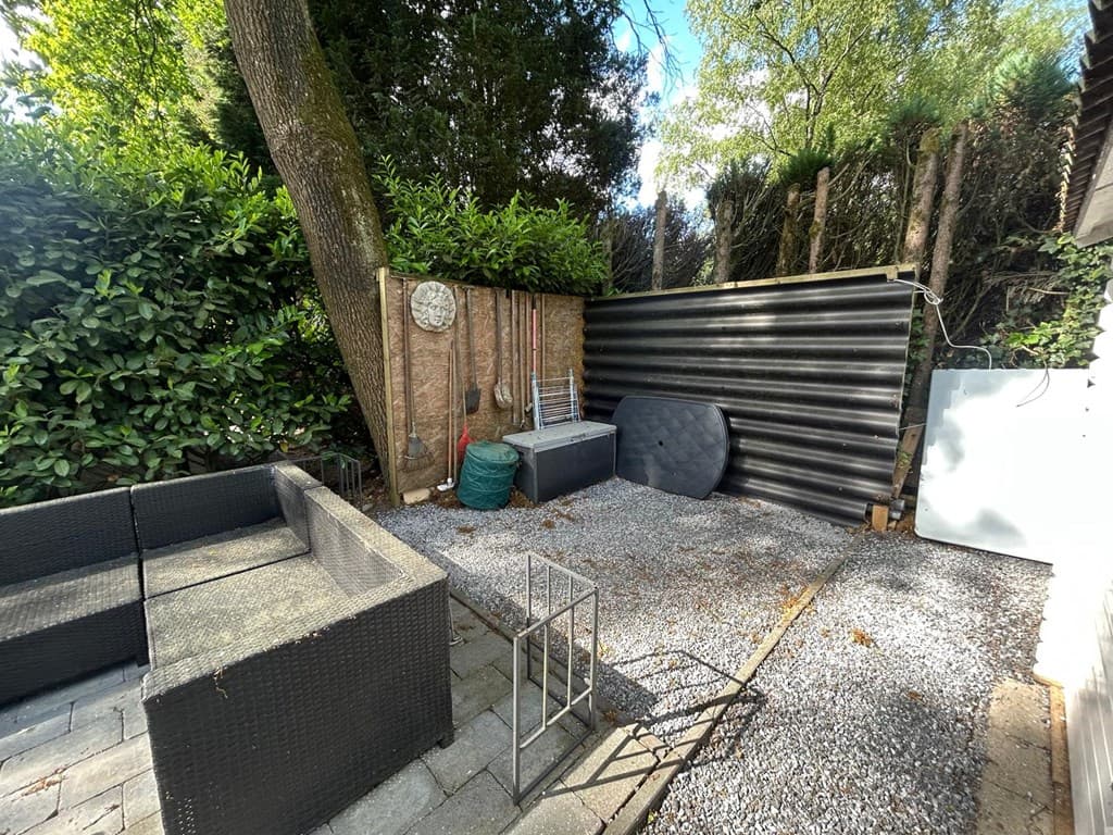 Terras met een zithoek van zwart wicker en grind ondergrond, omringd door groen en een schutting van houten panelen