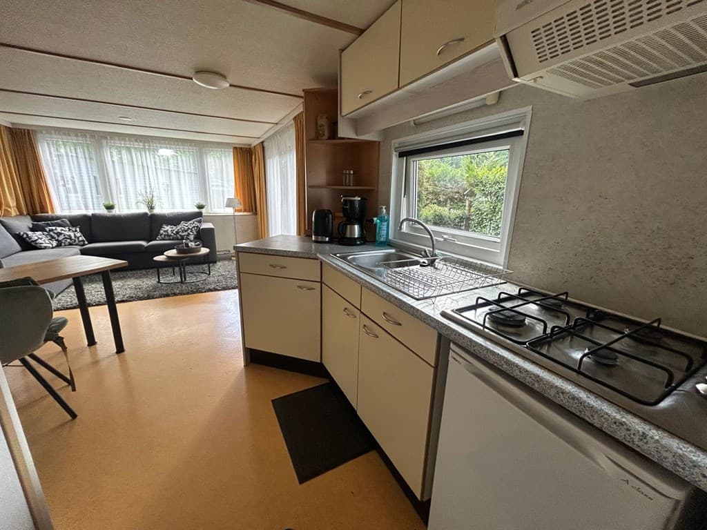 Hoekkeuken met gasfornuis, spoelbak en uitzicht op woonkamer met zithoek en grote ramen in vakantiewoning.