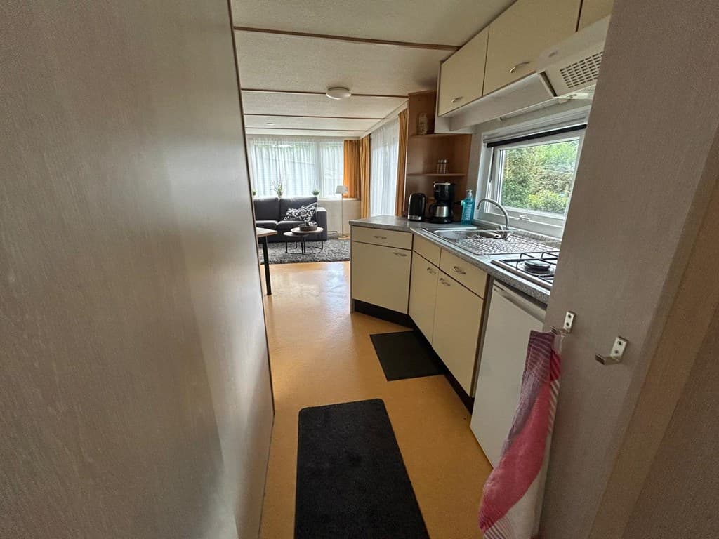 Keuken met gasfornuis en wasbak, uitzicht op een woonkamer met bank en natuurlijke lichtinval.