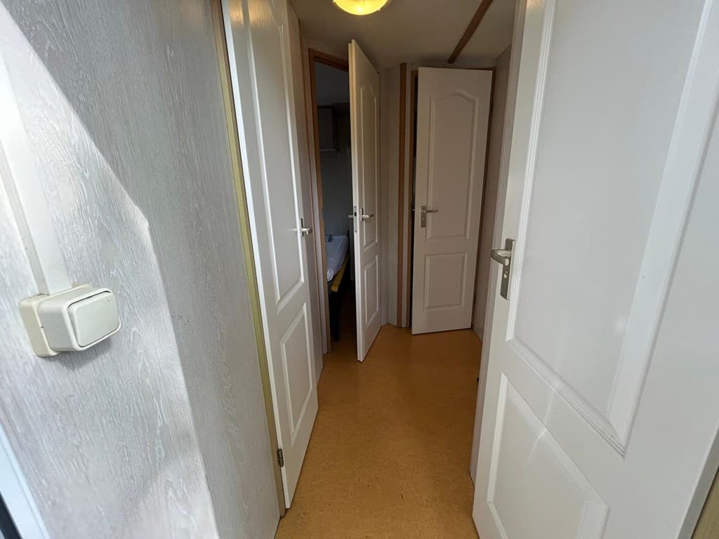 In een gang met deuren naar meerdere kamers en een lichte vloerbedekking.