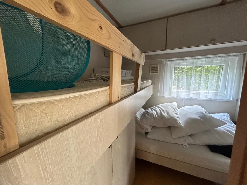 Slaapruimte met een hoogslaper, een bed en een raam met uitzicht op groen. Kussens liggen verspreid op het bed.