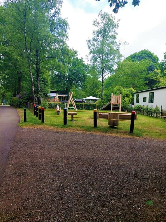 Speelplaats met houten speeltoestellen, omgeven door bomen en een pad in Bospark Ede