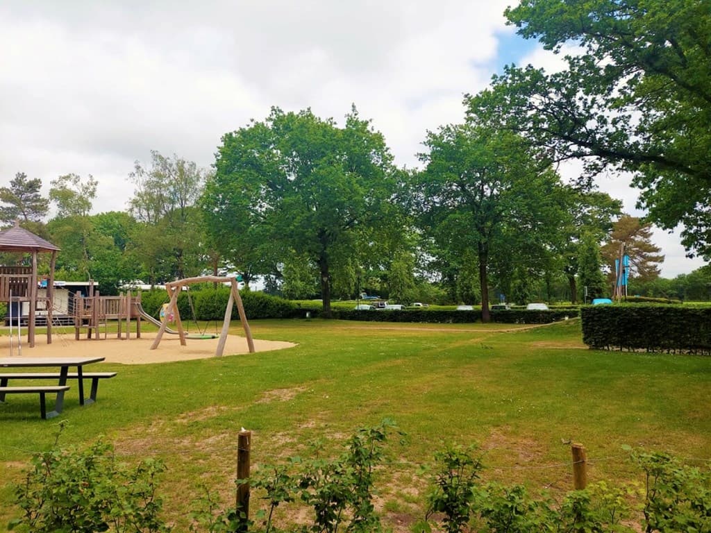 Speeltuin met schommels en een zandbak omringd door groene grassengebieden en bomen in Bospark Ede