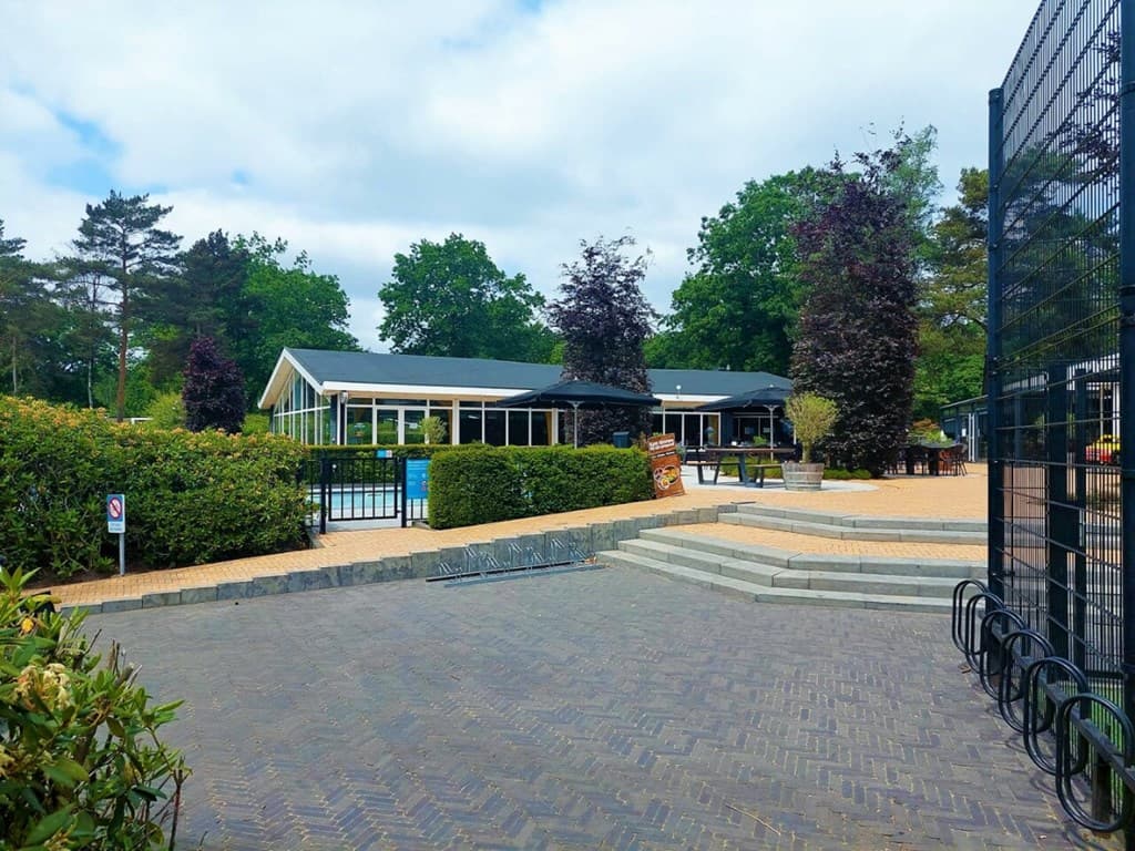 Receptiegebouw met grote ramen, omringd door groen en bestrating, bij het zwembad van Bospark Ede