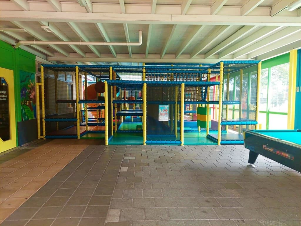 Speelruimte met kleurrijke klimtoestellen en netten, voorzien van een tafel voor biljart aan de rechterzijde.