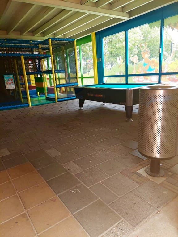 Speelruimte met kleurrijke wanden, een speeltoestel en een tafel naast een afvalcontainer op de vloer van een parkgebouw