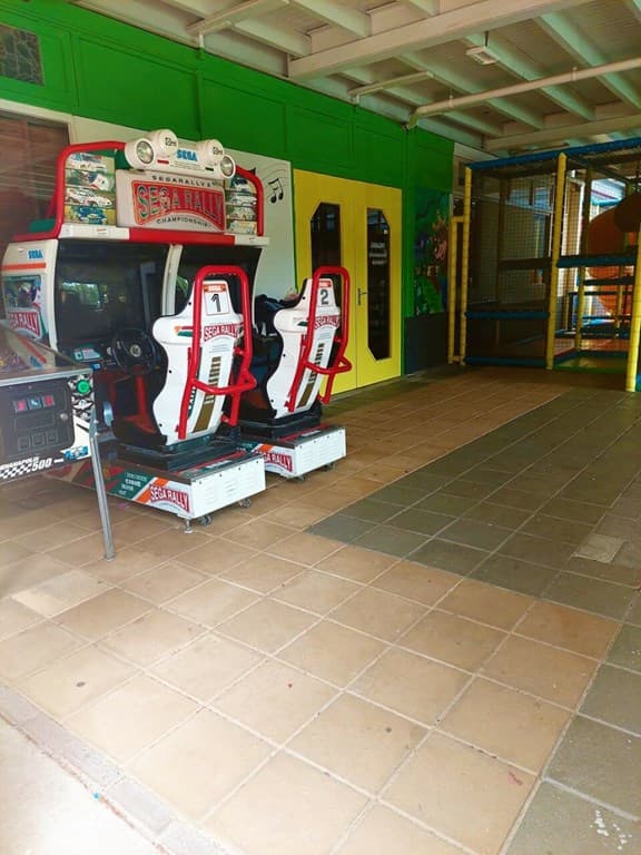 Twee arcade speelautomaten staan naast elkaar in een kleurrijke ruimte met een speelstructuur op de achtergrond