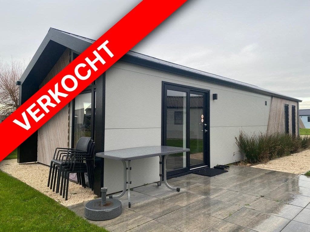 Moderne vakantiewoning met terras, tuinmeubels en een aangelegde tuin grenzend aan een betegeld pad.