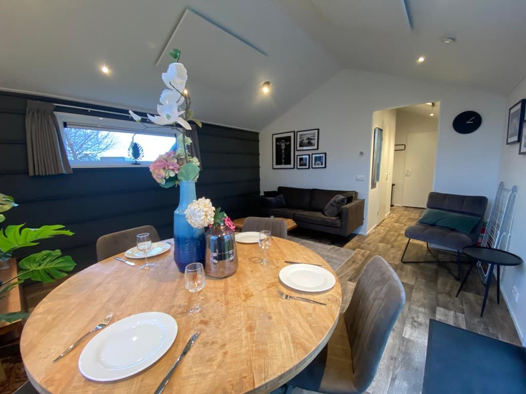 Eetkamer met een ronde houten tafel, stoelen, een bank en decoratieve planten en foto's aan de muur