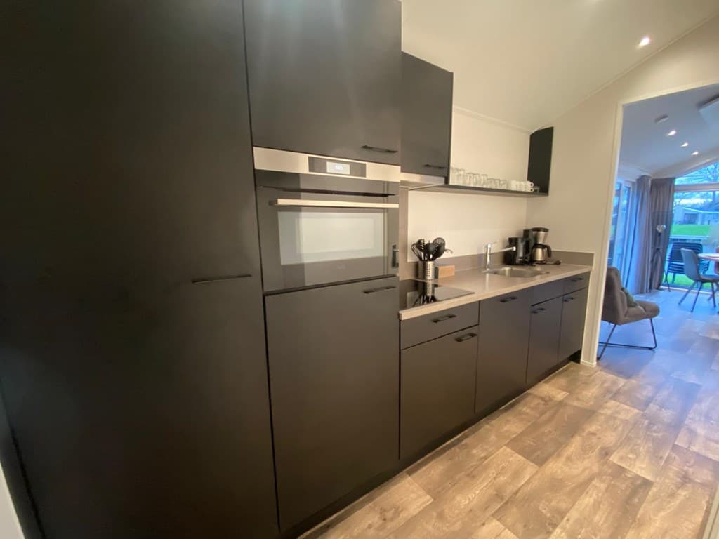 Moderne keuken met zwarte kasten, inbouwapparatuur en een koffiezetapparaat, uitzicht op de eetruimte.
