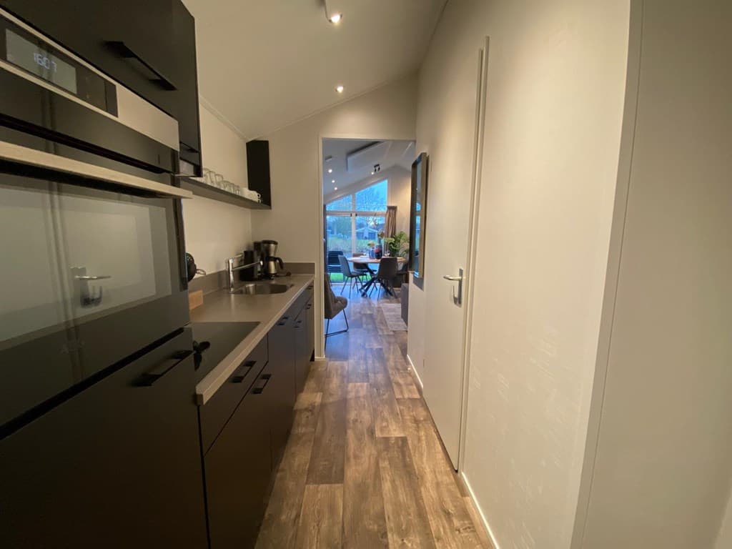 Uitzicht op een gang met een moderne keuken en toegang tot een lichte woonkamer met grote ramen