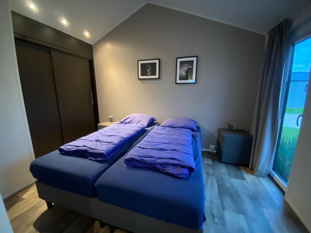 Sfeervolle slaapkamer met twee losse bedden, moderne inrichting en toegang tot een buitenterras.