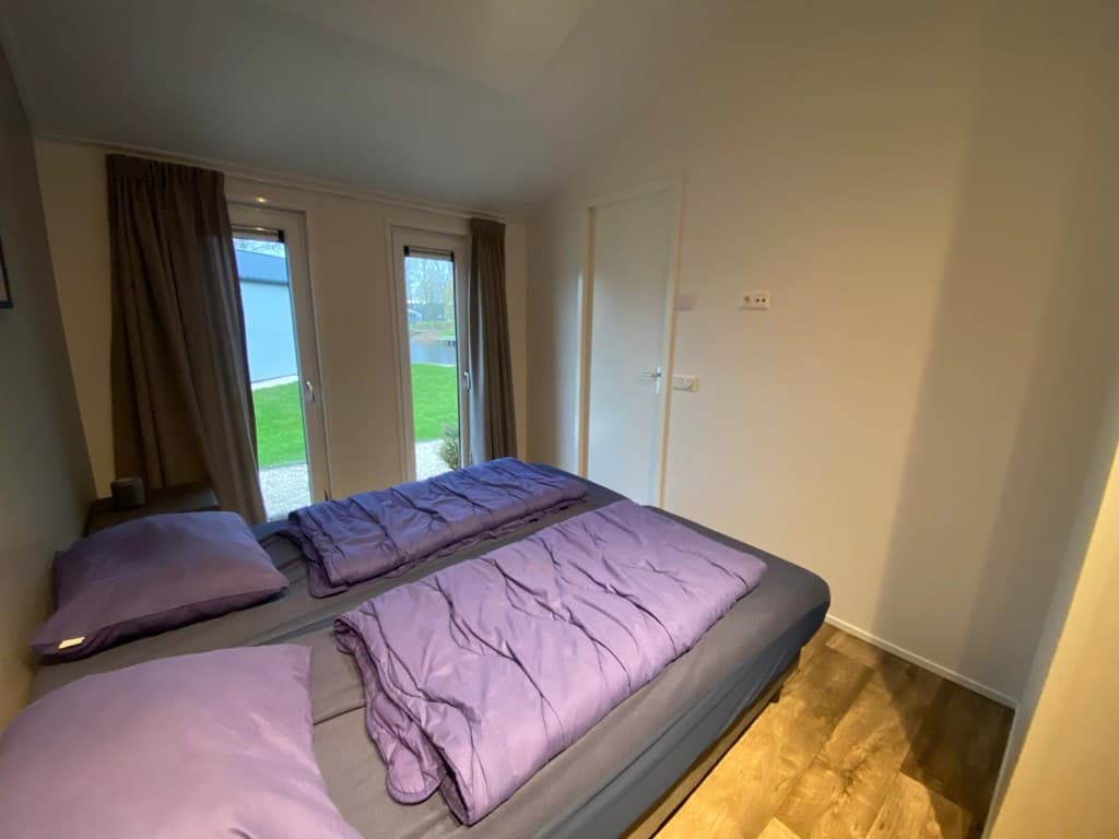 Slaapkamer met twee aparte bedden, paarse dekbedden en dubbele deuren naar buiten met uitzicht op de tuin.