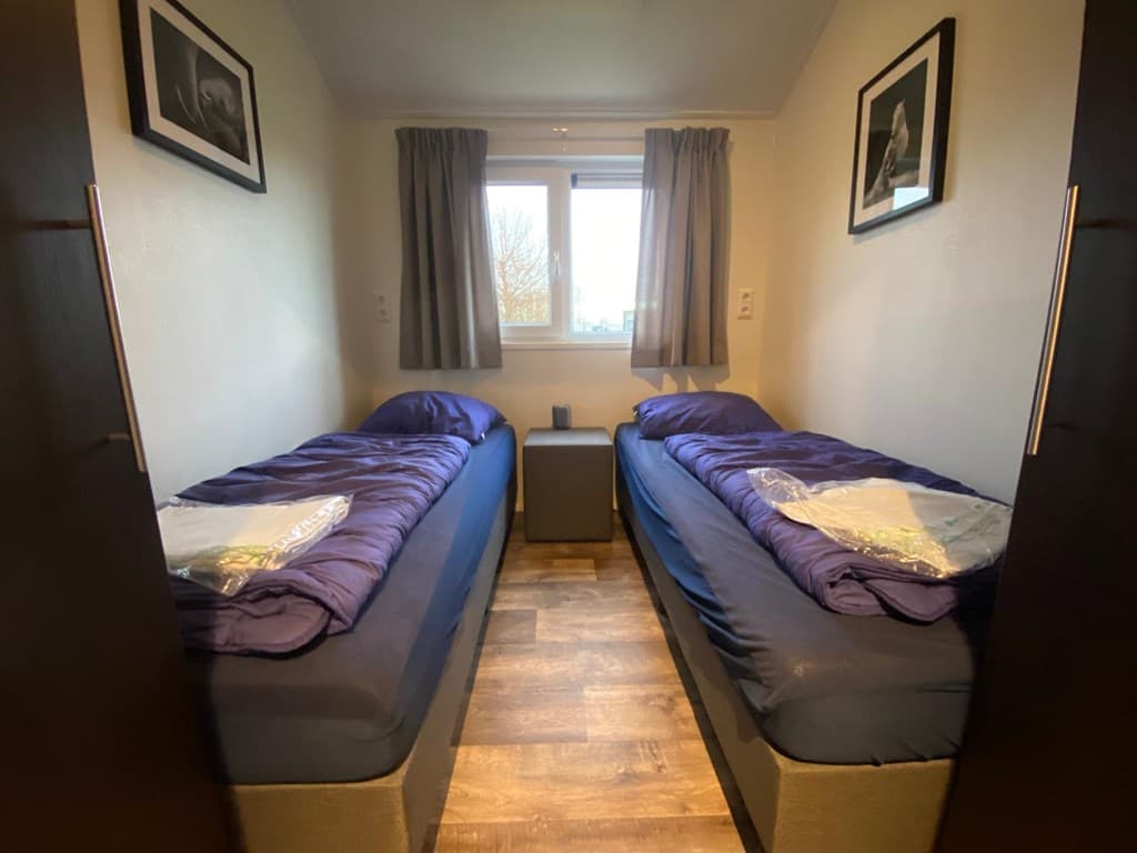 Slaapkamer met twee eenpersoonsbedden, een nachtkastje en raam met uitzicht naar buiten.