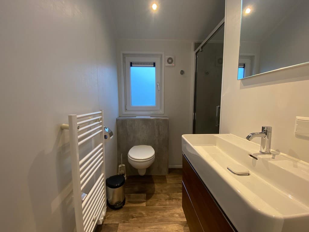 Moderne badkamer met wastafel, douche, toilet en handdoekenradiator, lichte kleuren en houten vloer