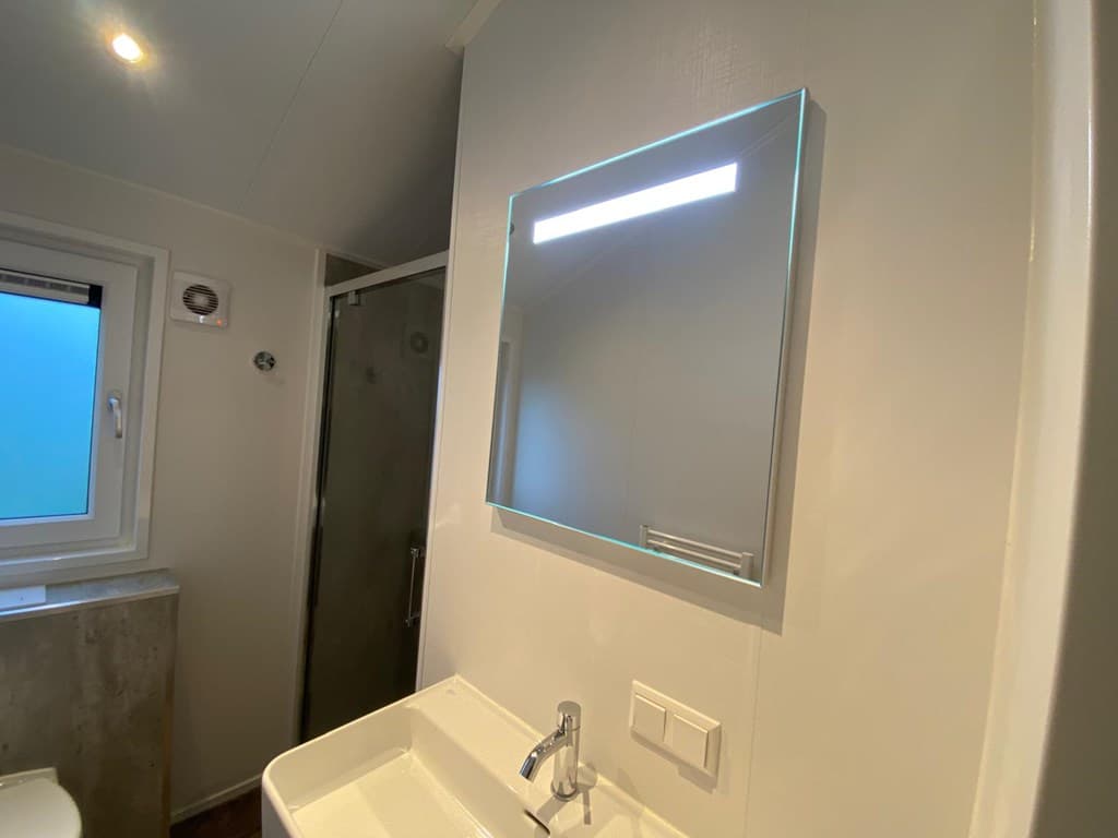 Lichte badkamer met een wastafel, spiegel met verlichting en douchecabine zichtbaar