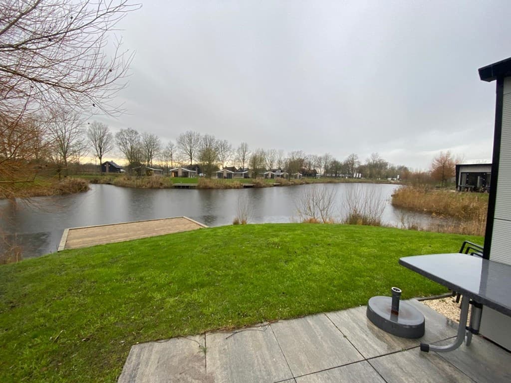 Uitzicht over de vijver met riet en bomen, vakantiehuizen zichtbaar aan de overkant met een groene graszone ervoor